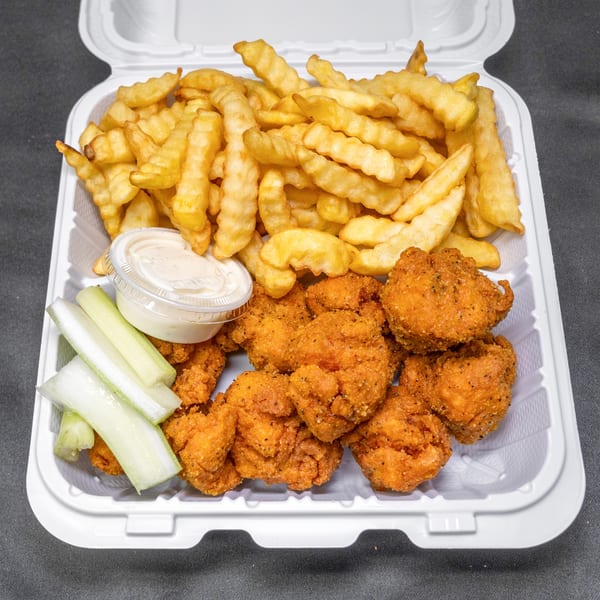 Takeout container with crispy boneless chicken, crinkle-cut fries, celery sticks, and dipping sauce.