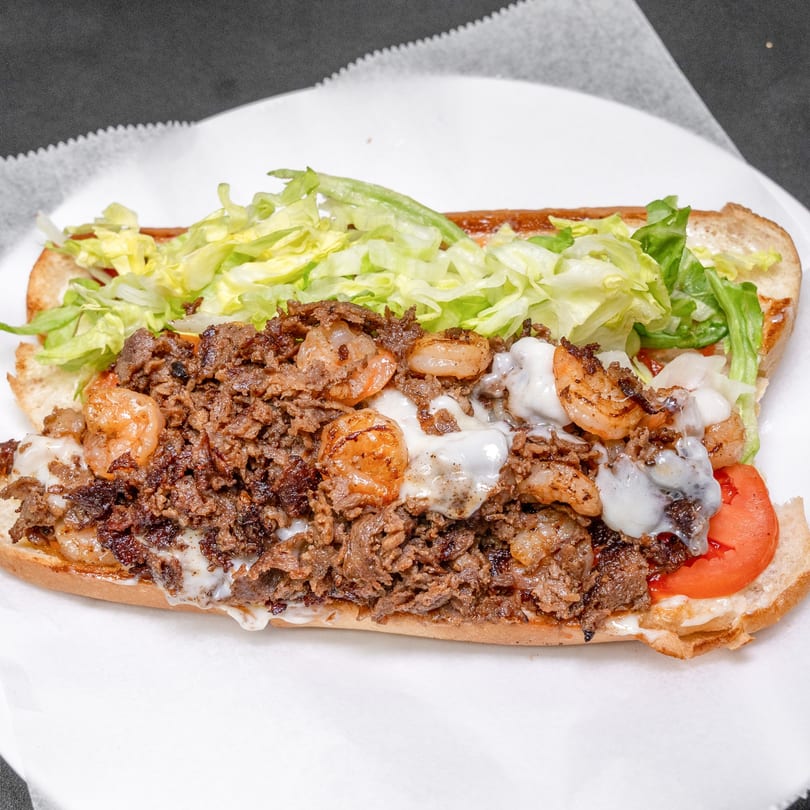 A large sub sandwich filled with steak, shrimp, melted cheese, lettuce, and tomato.