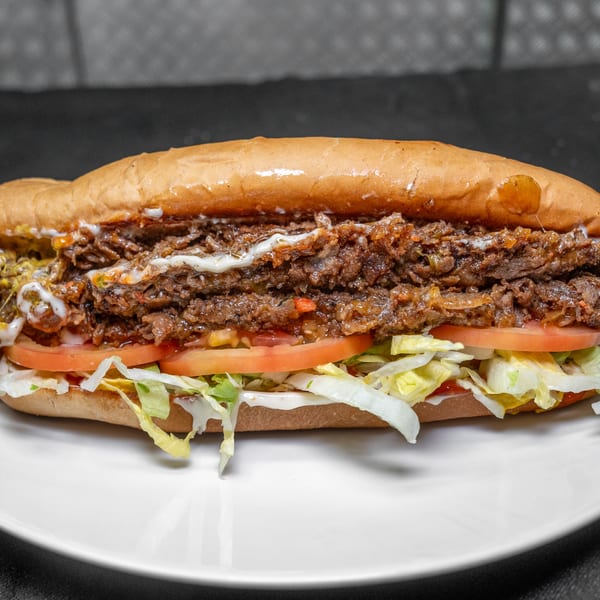 Hearty sub sandwich with shredded beef, tomatoes, lettuce, and creamy sauce on a white plate.