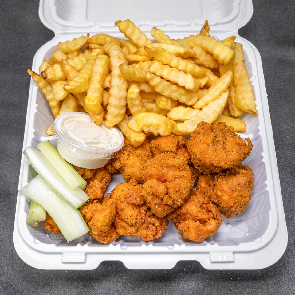 Takeout container with crispy fried chicken, crinkle-cut fries, celery sticks, and dipping sauce.