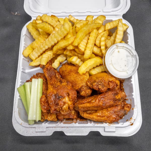 Spicy chicken wings, crinkle-cut fries, celery sticks, and ranch dip in a white takeout container.