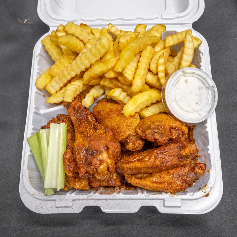 Spicy chicken wings, crinkle-cut fries, celery sticks, and ranch dip in a white takeout container.